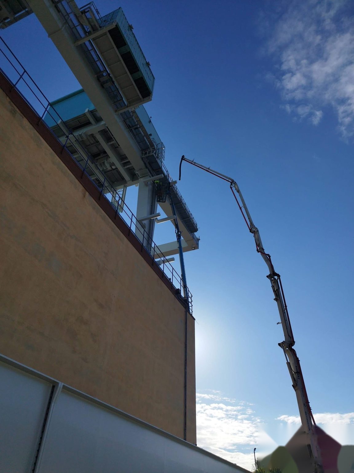 Bras de pompe à béton déployé en hauteur contre un ciel bleu, le long d'un bâtiment